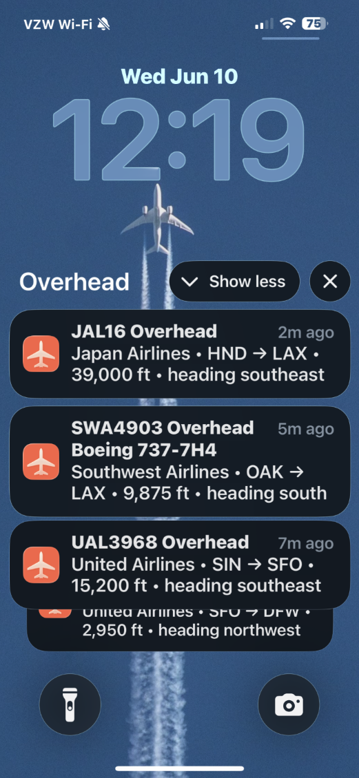 Overhead lock screen showing real-time flyover notifications — Japan Airlines HND to LAX at 39,000 ft, and other flights passing overhead